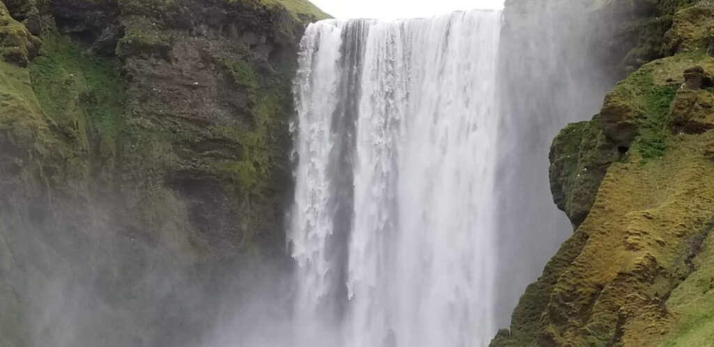 Waterfall cascading between mossy cliff faces, with mist rising and rugged green rocks on both sides.