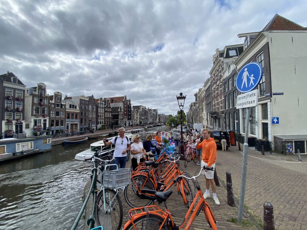 Bikes lined up along a canal with historic townhouses and a cloudy sky in the background (urban European scene).