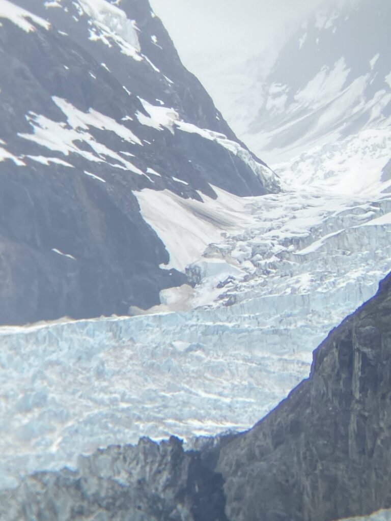 Snowy alpine valley with steep rocky cliffs and a glacier extending across the lower foreground.